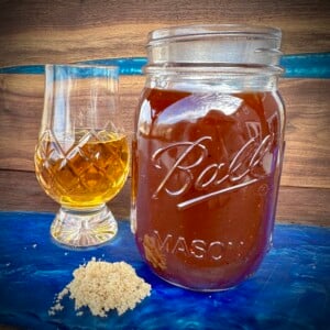 bourbon bbq sauce in a mason jar with a glass of bourbon and a pile of brown sugar.