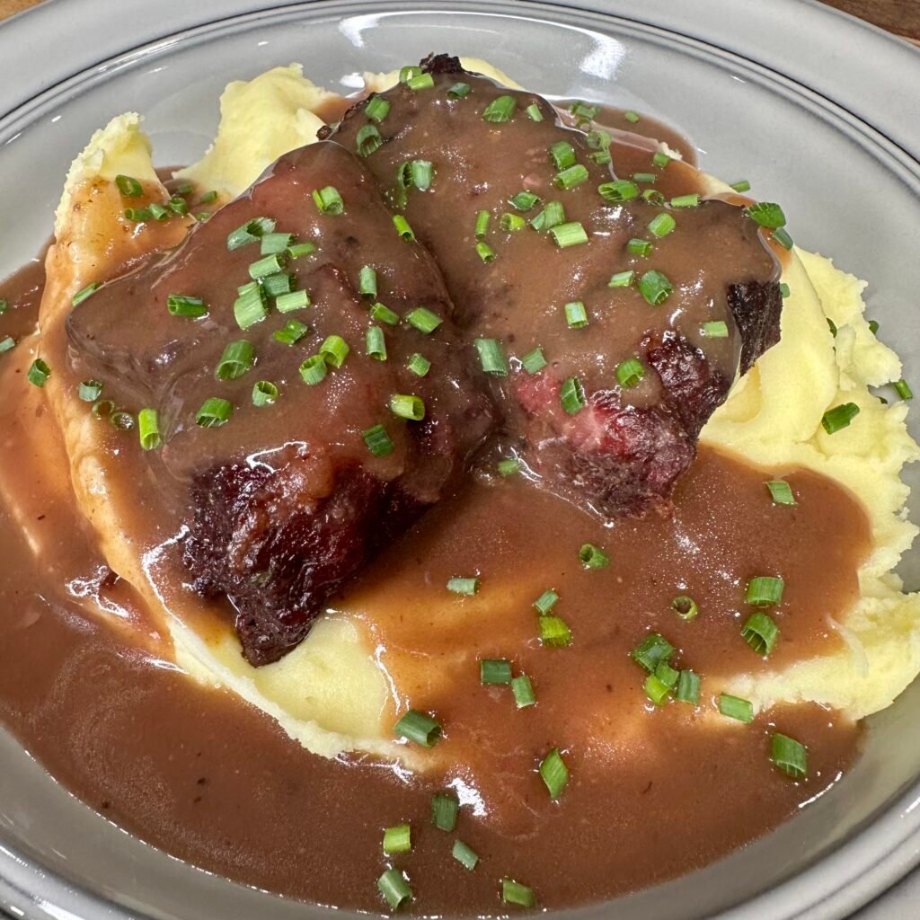 braised short ribs covered in gravy on top of a pile of mashed potatos.