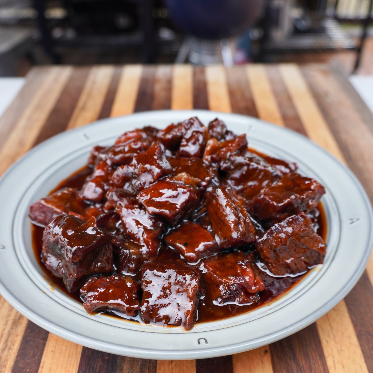 A white plate full of sweet and spicy burnt ends on a wooden cutting board.