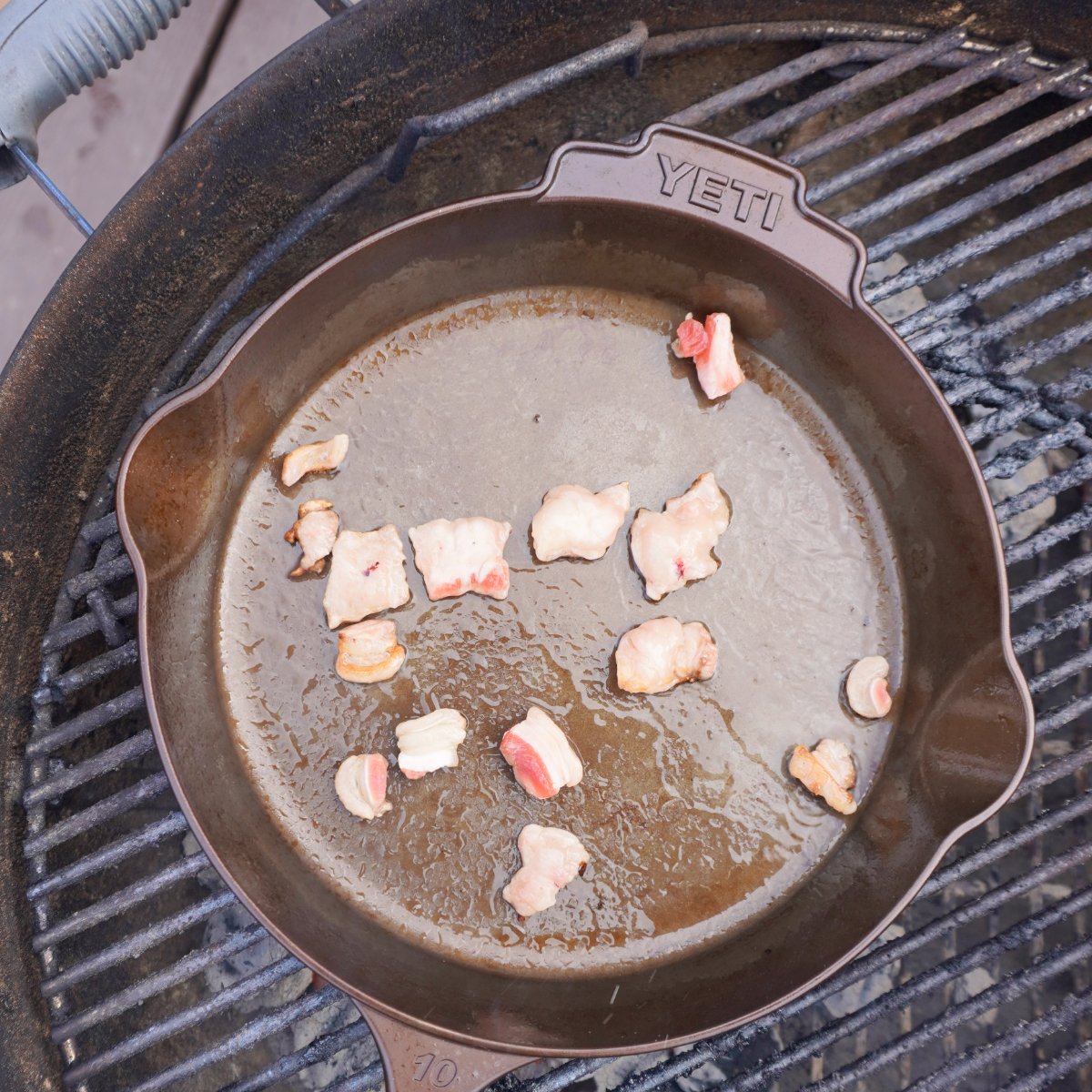 Beef fat melting on a hot cast iron skillet over hot charcoal.