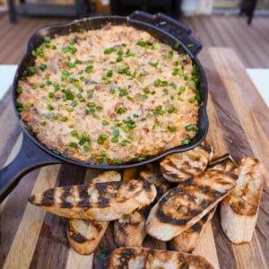 Smoked Cheese steak dip in a cast iron skillet with a side of toasted bread all on a wooden cutting board.