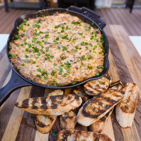 Smoked Cheese steak dip in a cast iron skillet with a side of toasted bread all on a wooden cutting board.