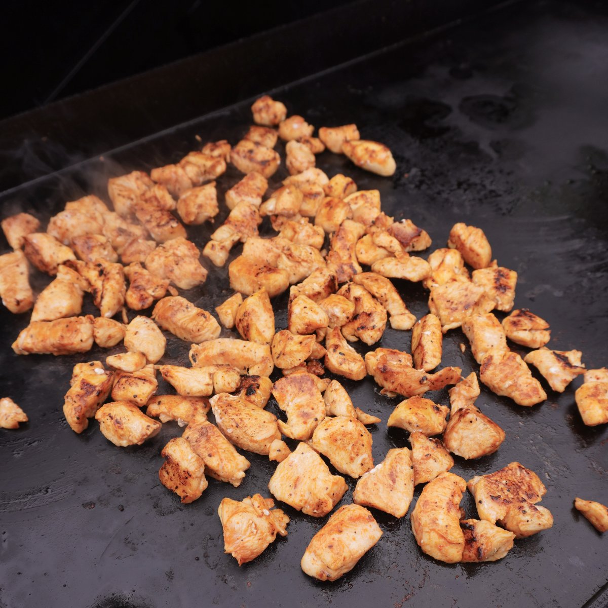 Grilled cubed chicken on a griddle top.