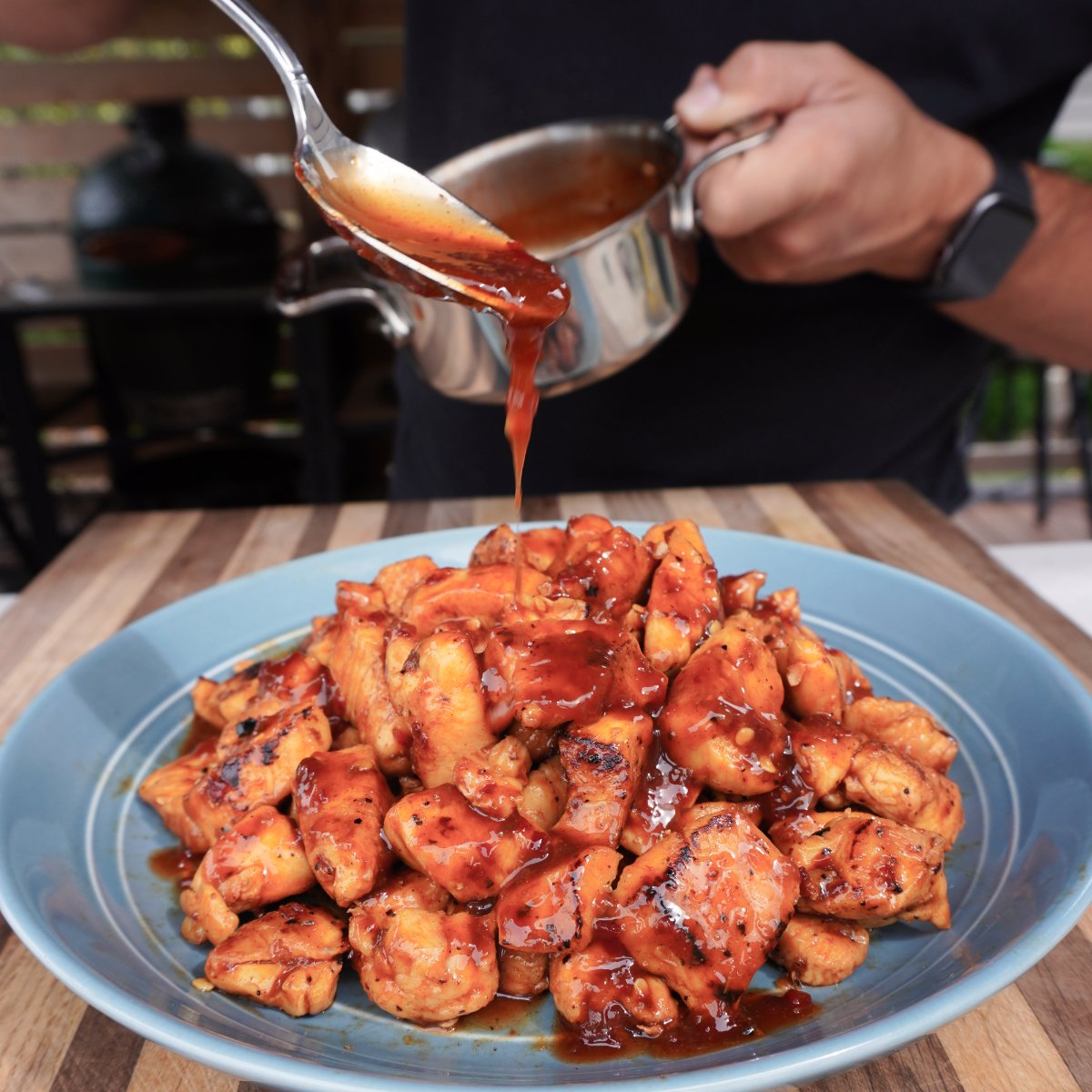 Sauce pouring over the grilled sweet chili chicken bites plated on a deep blue plate on top of a cutting board.