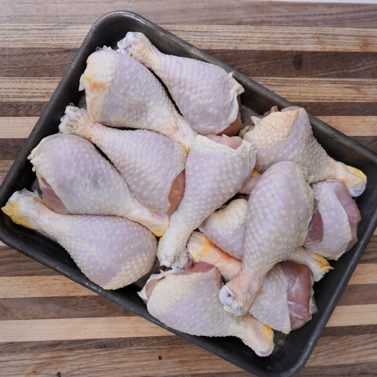 Raw chicken drumsticks on a metal tray.