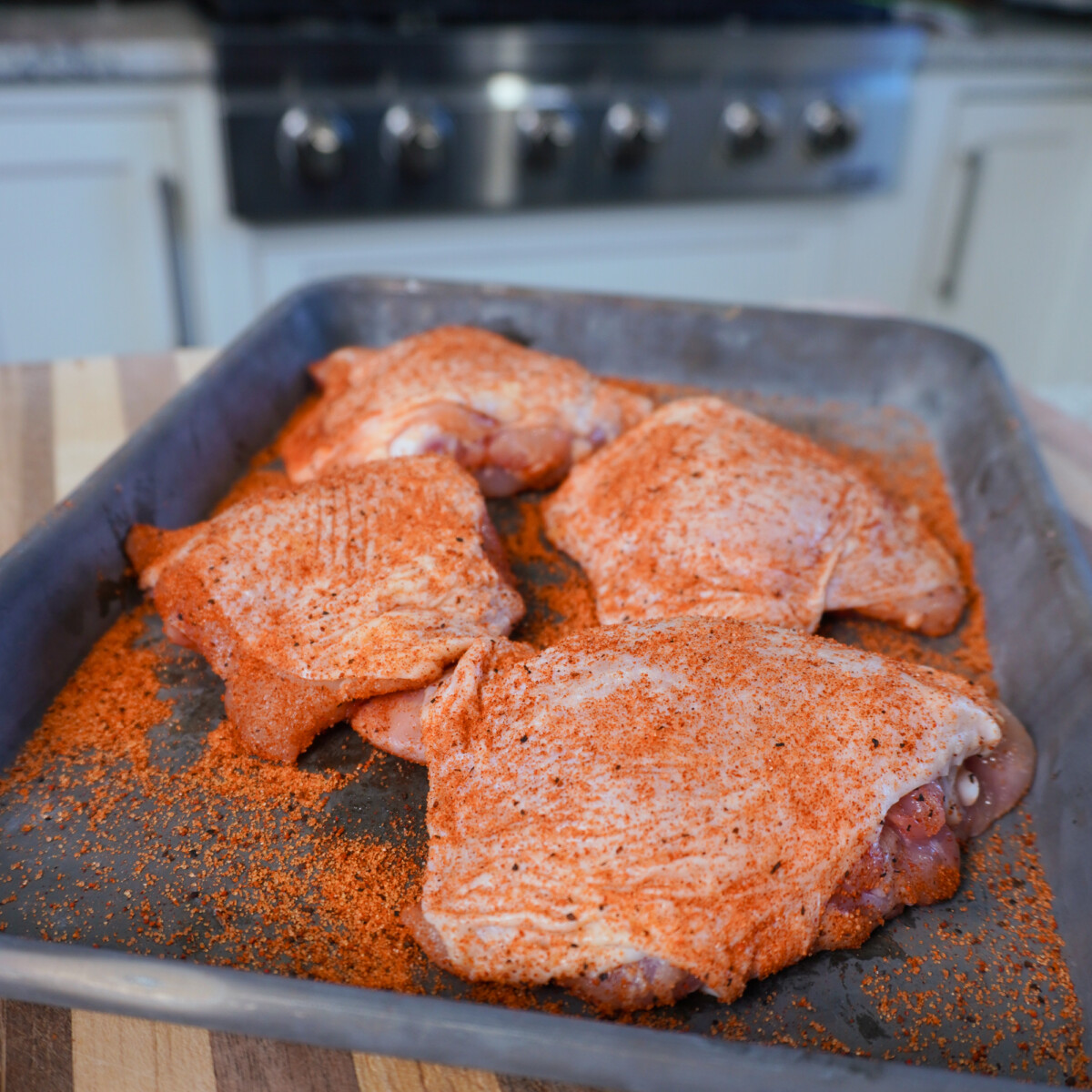 Seasoned chicken thighs on metal sheet.