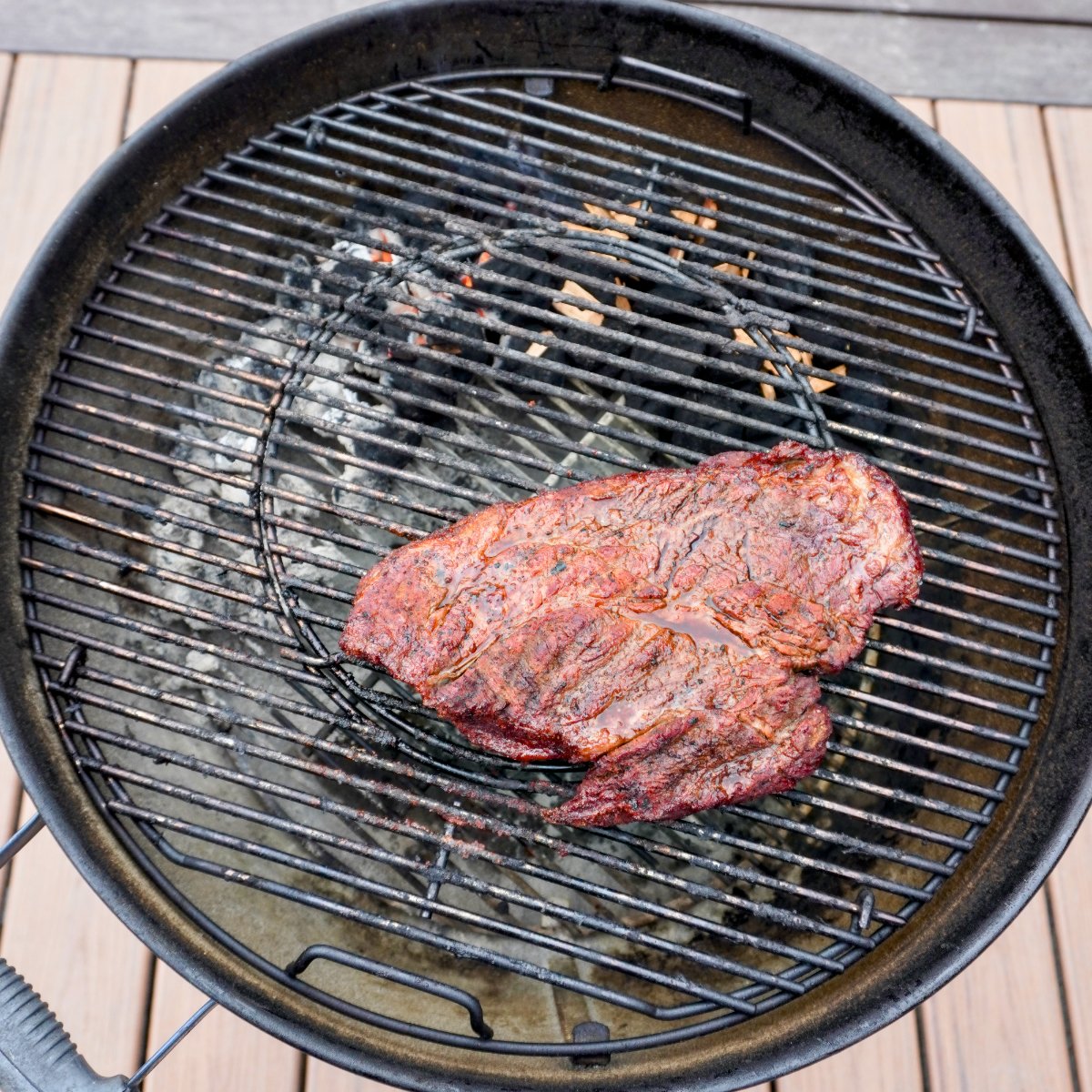Chuck roast smoking on a charcoal grill.