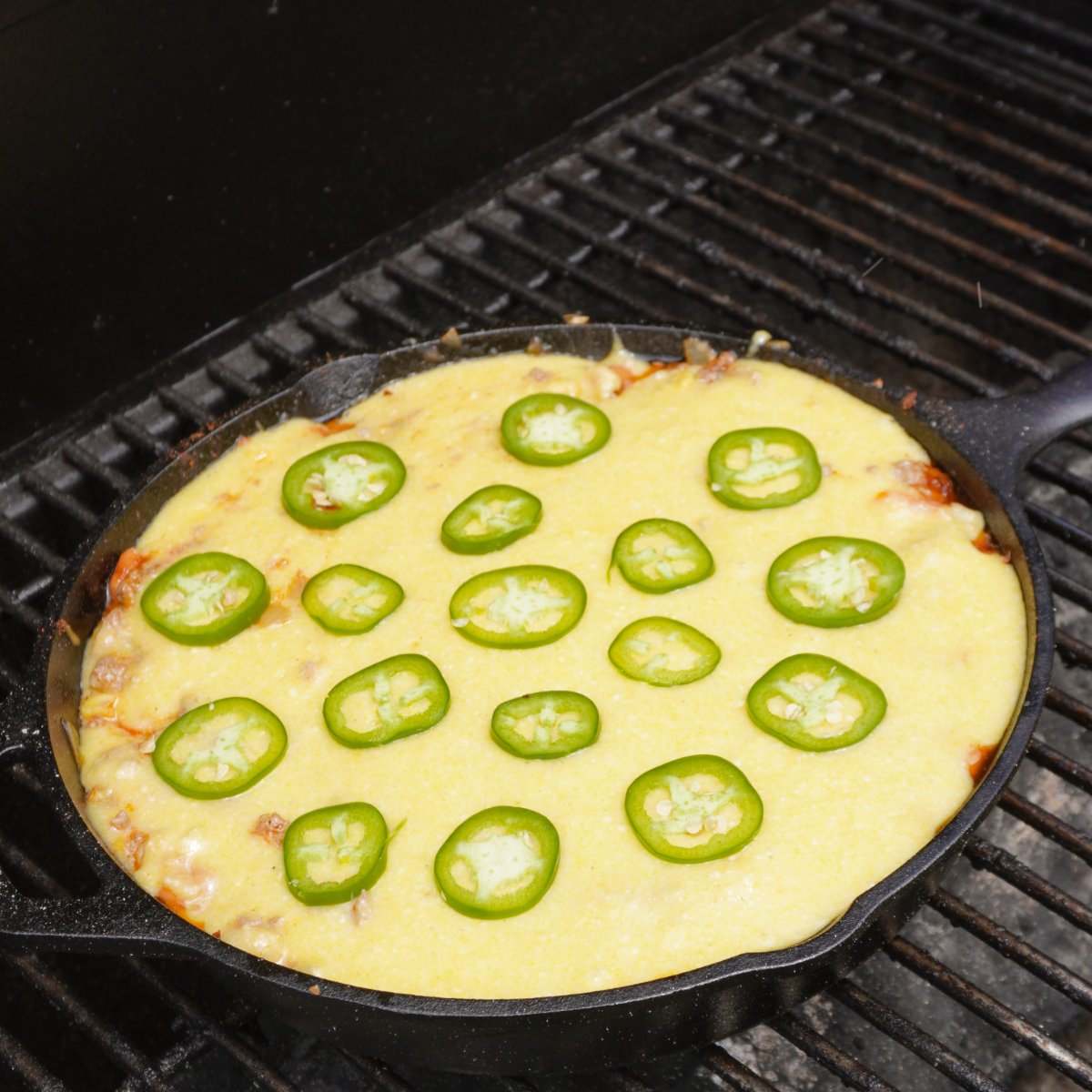 poured cornbread mix garnished with sliced jalapeno's over the cowboy meat mix in a cast iron skillet on the grill
