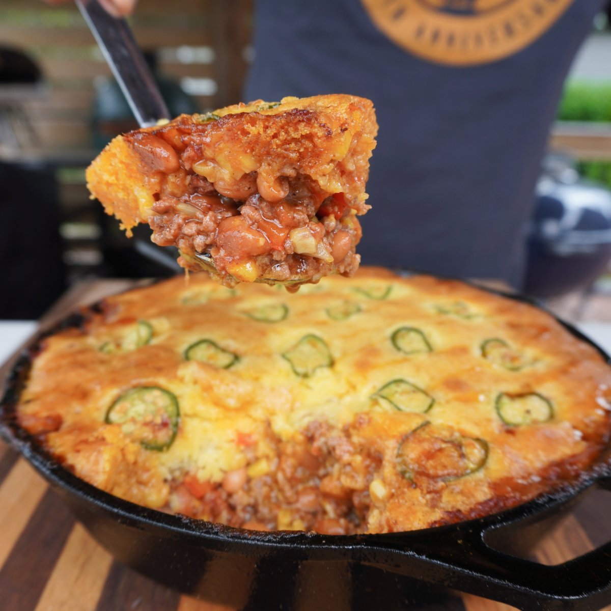 Smoked cornbread cowboy casserole with a spooned out slice showing the inside all in a cast iron skillet