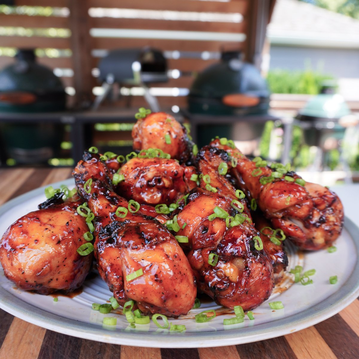 A pile of grilled chicken drumsticks in Dr Pepper BBQ sauce on a place with grills in the background.
