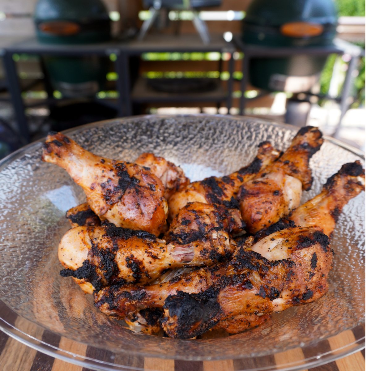 Grilled chicken drumsticks ready to be tossed in Dr. Pepper BBQ sauce on a clear bowl on a wooden cutting board.