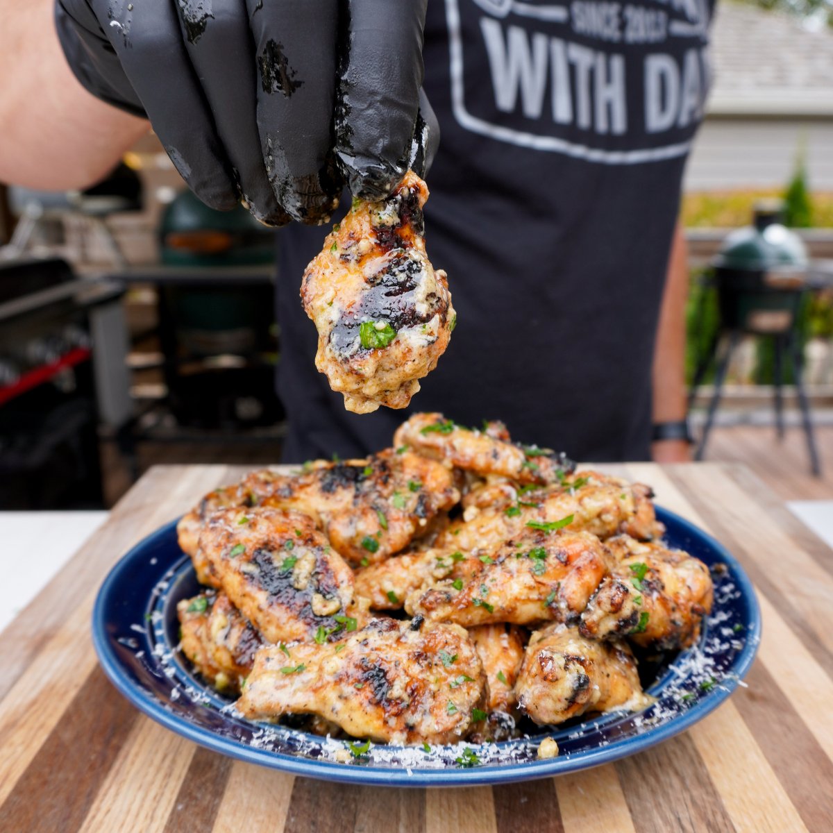 cooked garlic parmesan wings on a blue plate, one wing being raised. 