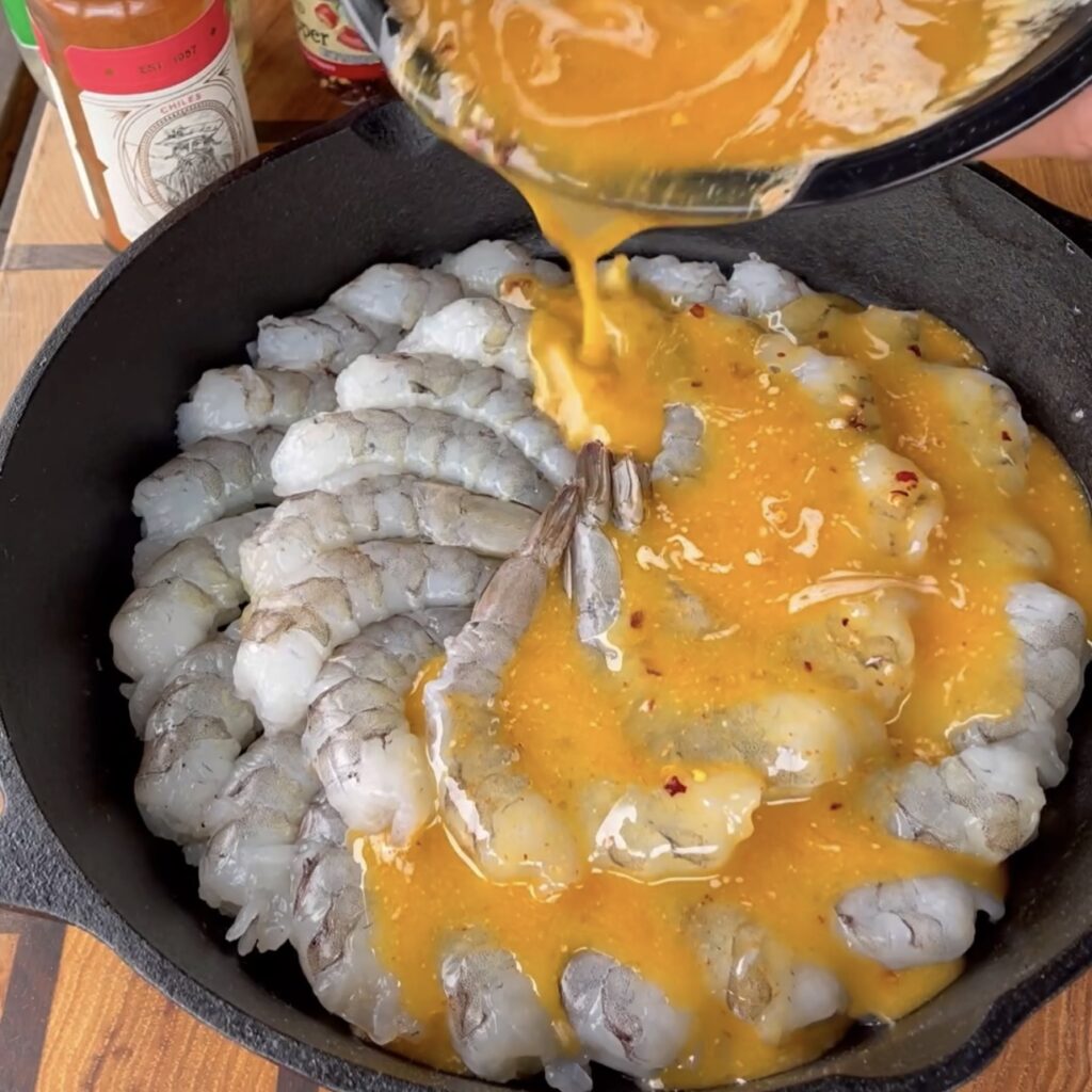 Butter and garlic mixture being poured over the shrimp in a cast iron skillet. 