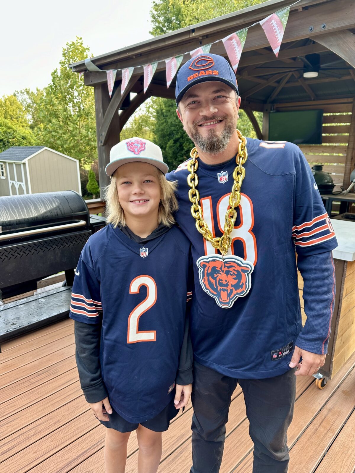 father and son standing in their backyard, wearing football gear. 