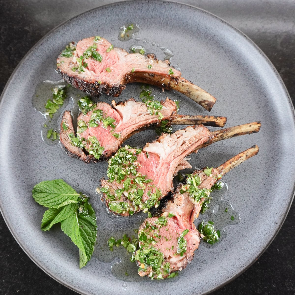 smoked lamb chops with mint chimichurri sauce on a grey serving plate with a side of fresh mint leaves
