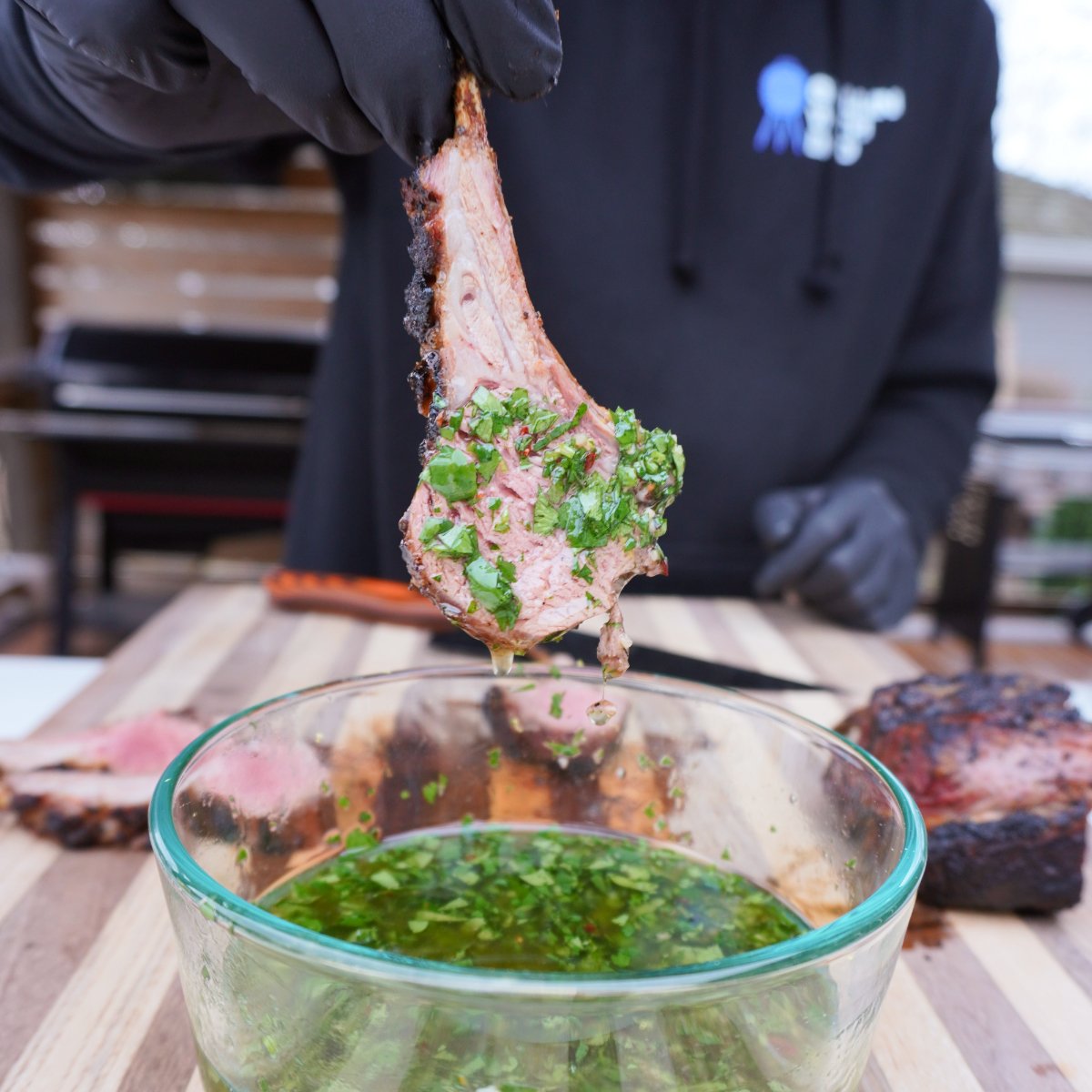 smoked and sliced rack of lamb dipped in a mint chimichuri sauce from a clear bowl.