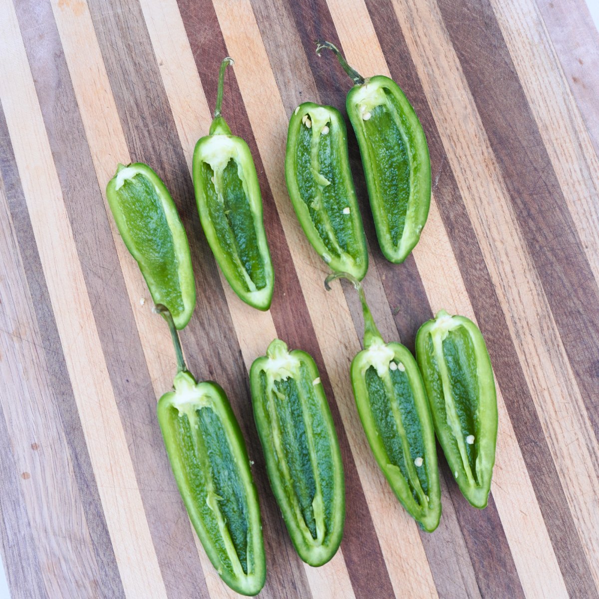 sliced in half, pitted jalapenos on a cutting board.