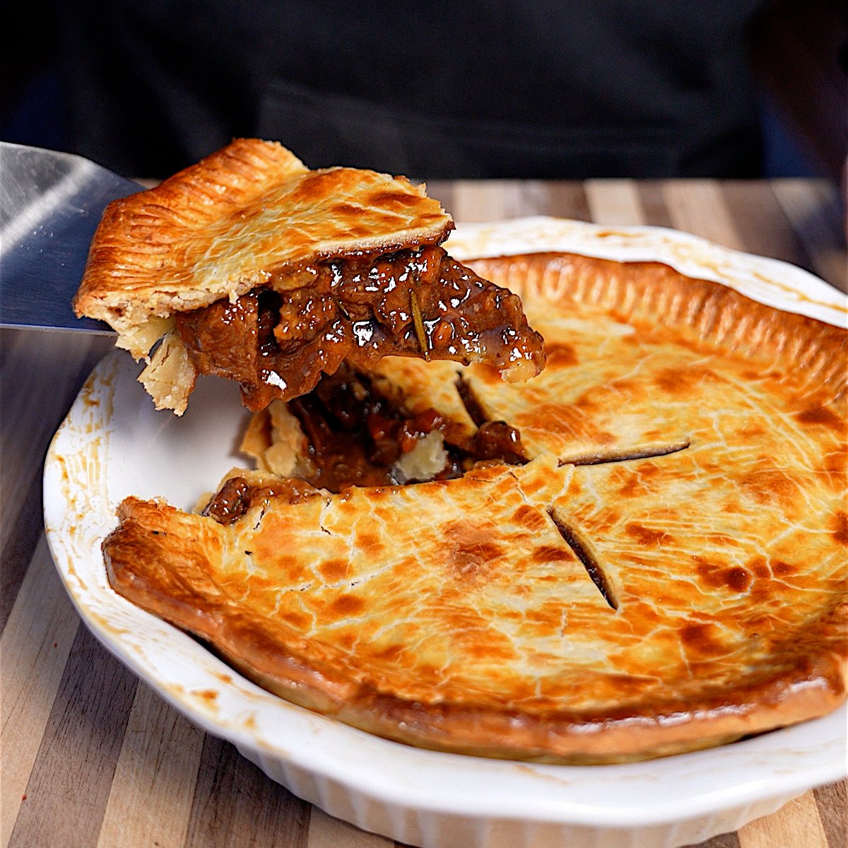 smoked meat pie with a cut up slice showcasing the meaty gravy feeling in a while pie dish.