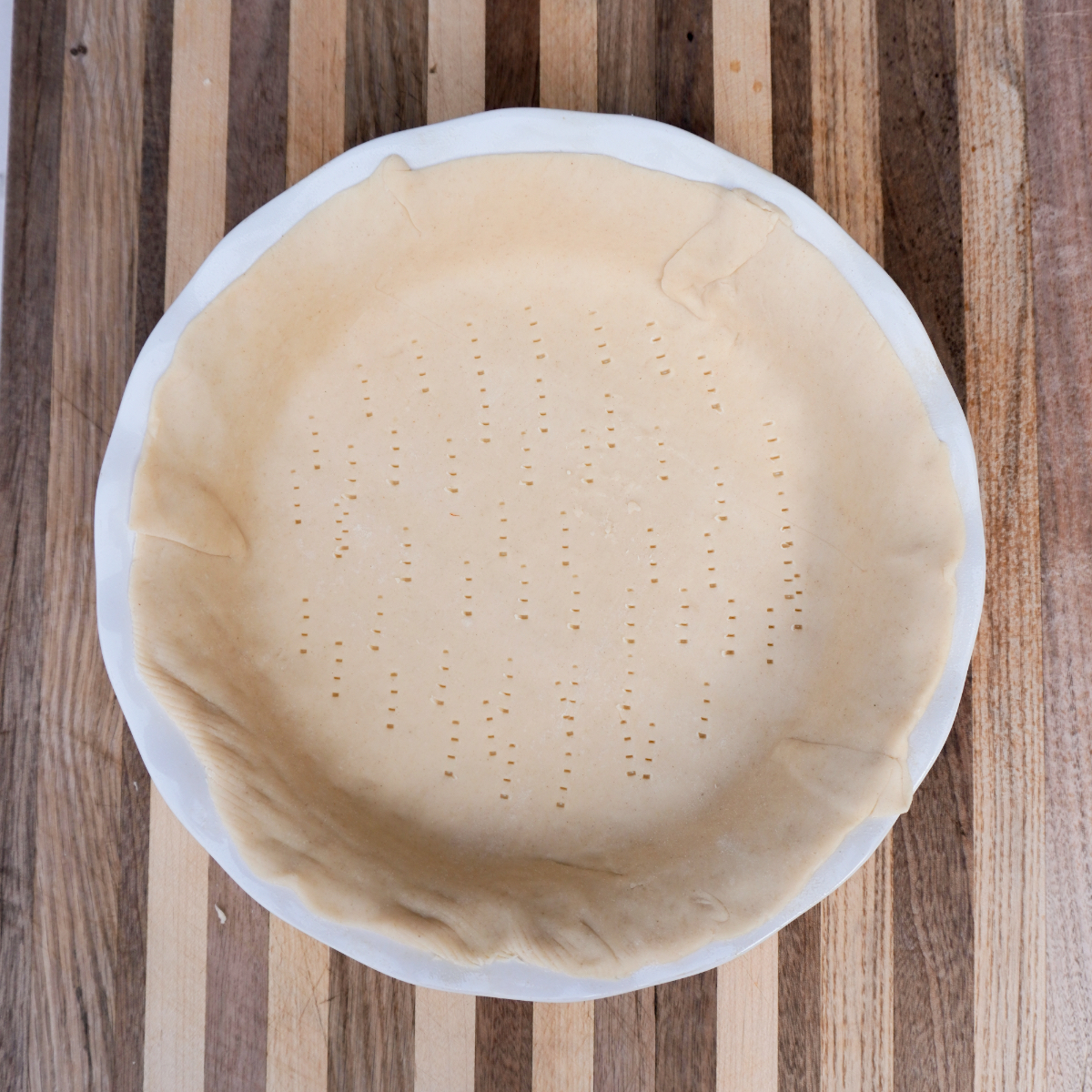 raw pie crust molded in a white pie bowl on a wooden cutting board.