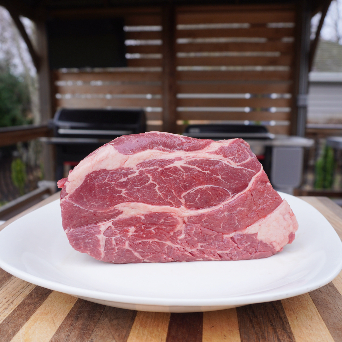 raw chuck roast on a white plate place on a wooden cutting board.