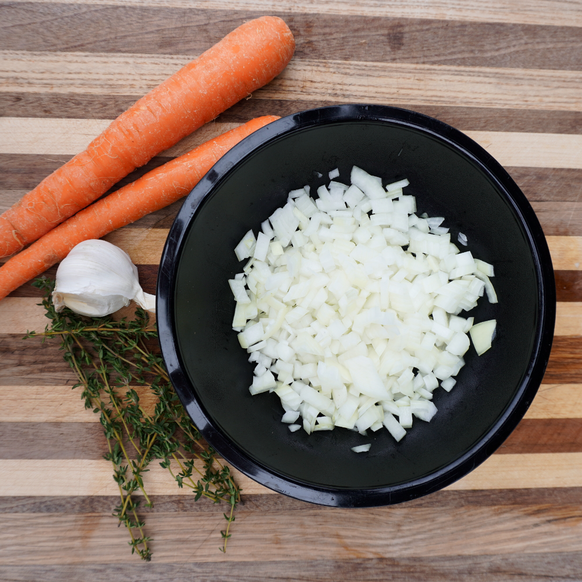 smoked meat pie gravy ingredients with a chopped yellow onion in a black bowl all placed on a wooden cutting board.