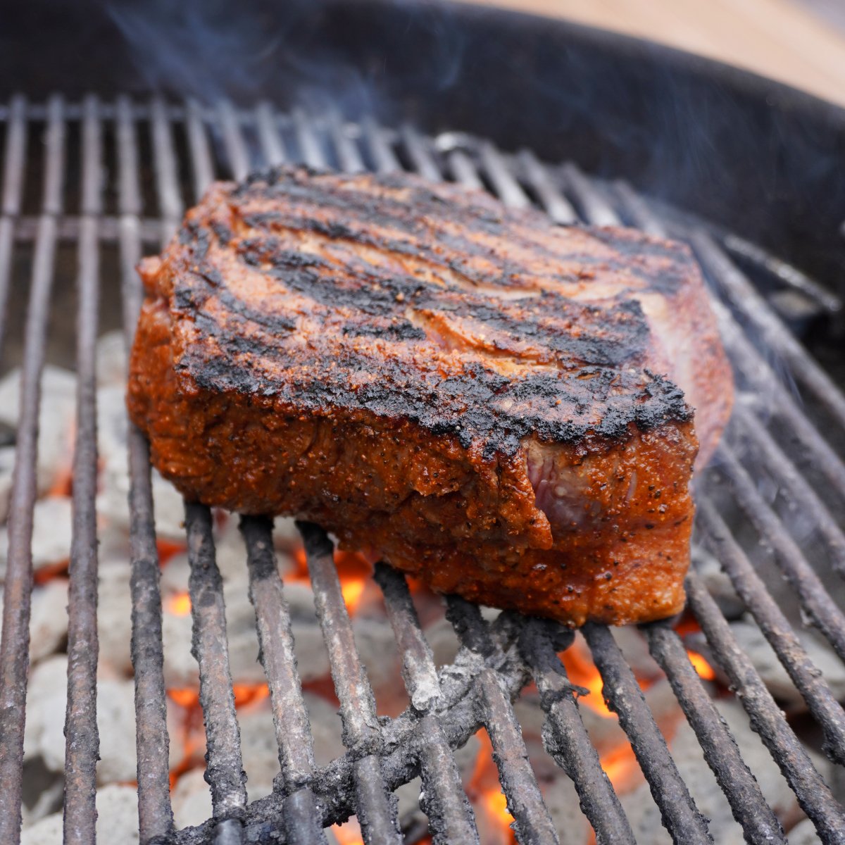 perfectly grilled chuck roast placed on grill grates over hot charcoal.
