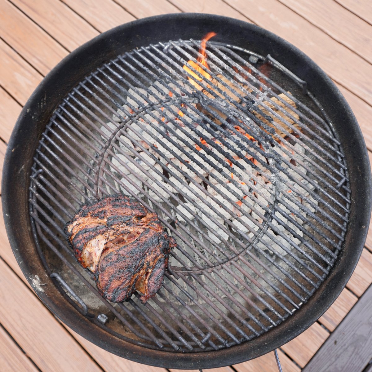 a charcoal grill set up for dual zone cooking with hot charcoal and wood chunks on the right side and a smoking chuck roast on the left.