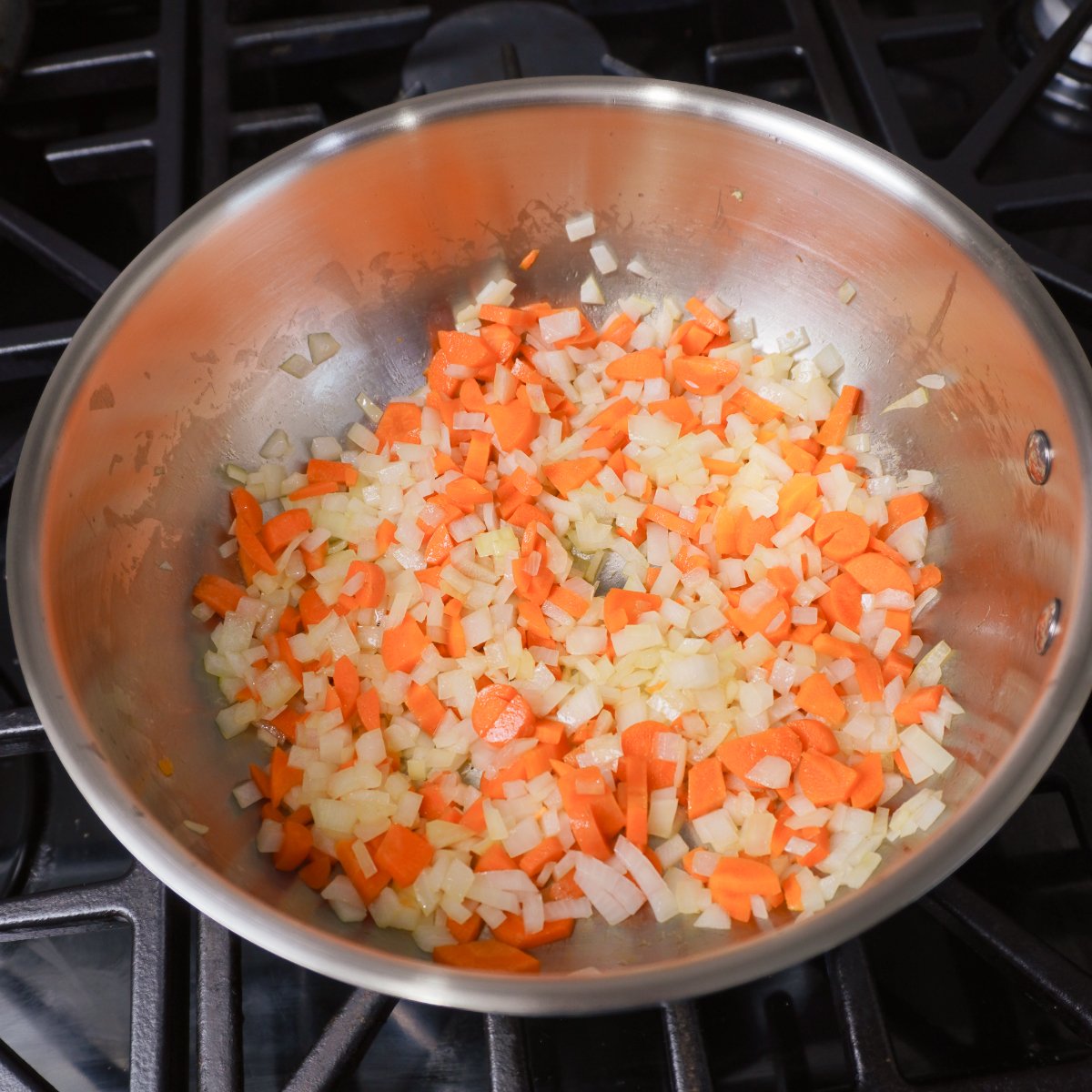 sauted onion, carrots and garlic in a metal saucepan on the stove top.