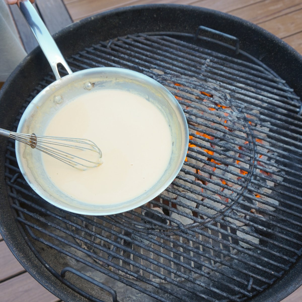 Nacho cheese sauce in a sauce pan directly over hot charcoal on a grill.