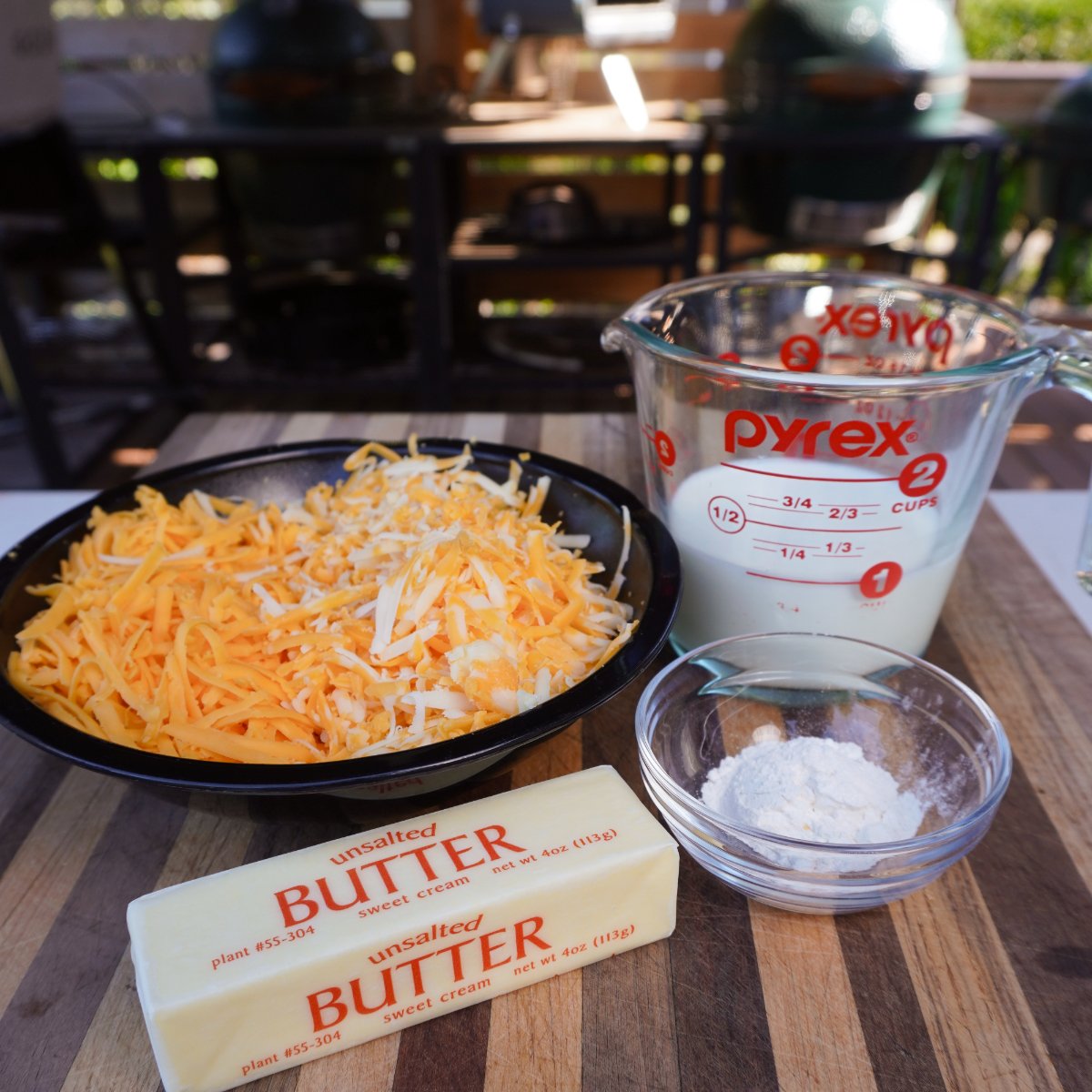 shredded cheese, milk, butter and flour ingredients for a cheese sauce on a cutting board.