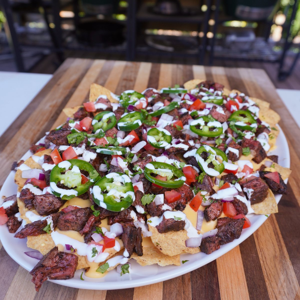 Cheesy steak nacho plate filled with chips, steak, veggies and other toppings on a cutting board.