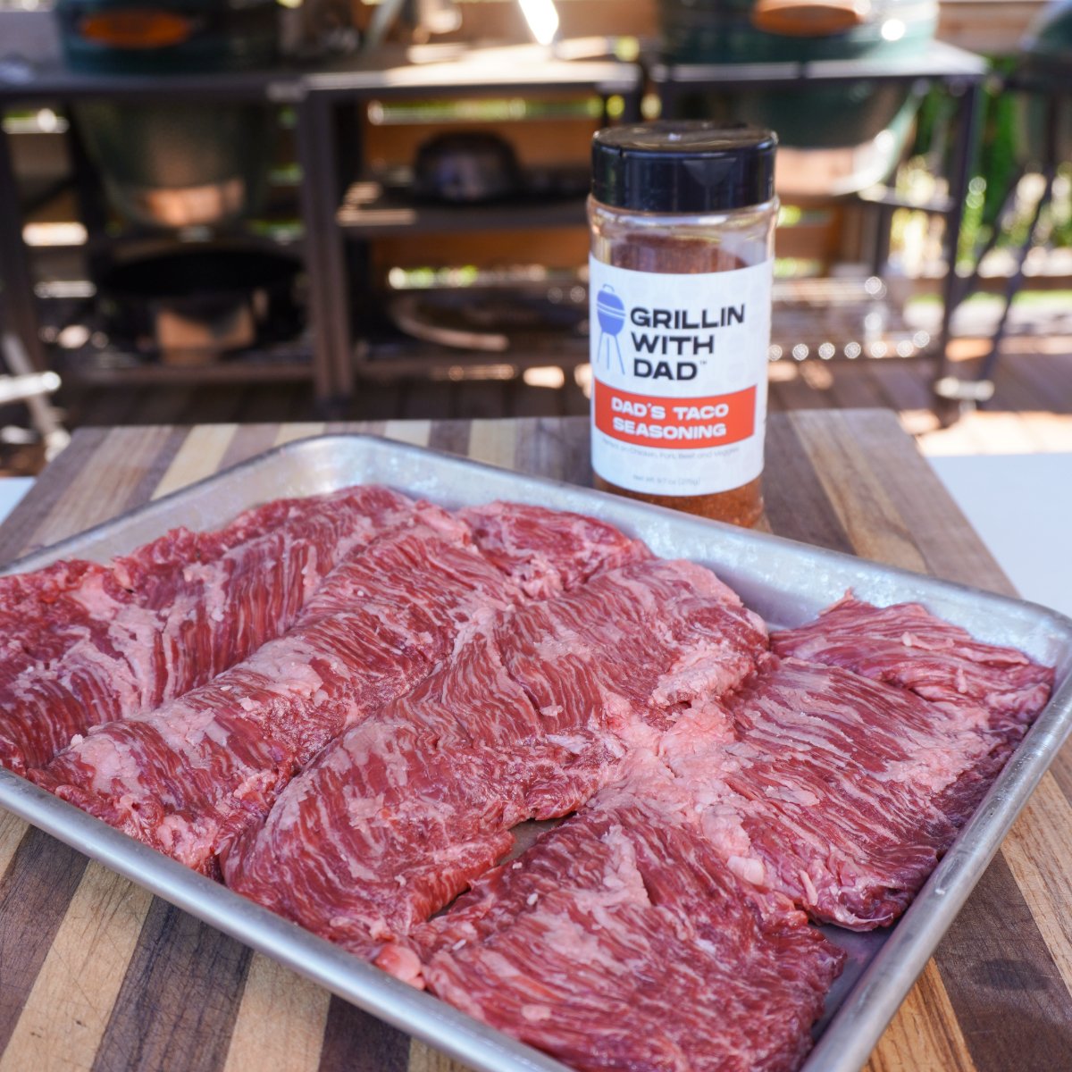 Raw skirt steak on a metal tray with a bottle of taco seasoning beside it.