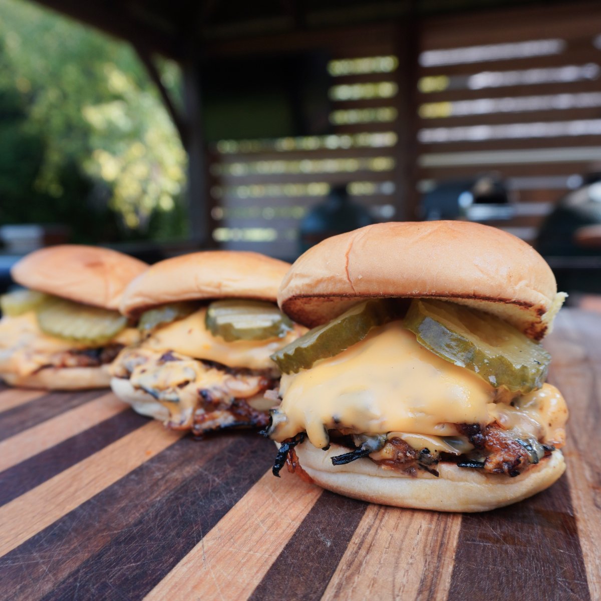 3 fully assembled Oklahoma Onion Burgers on a wooden cutting board.