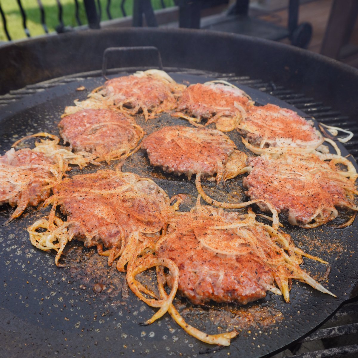 Seasoned smashed beef and onion patties on a griddle.