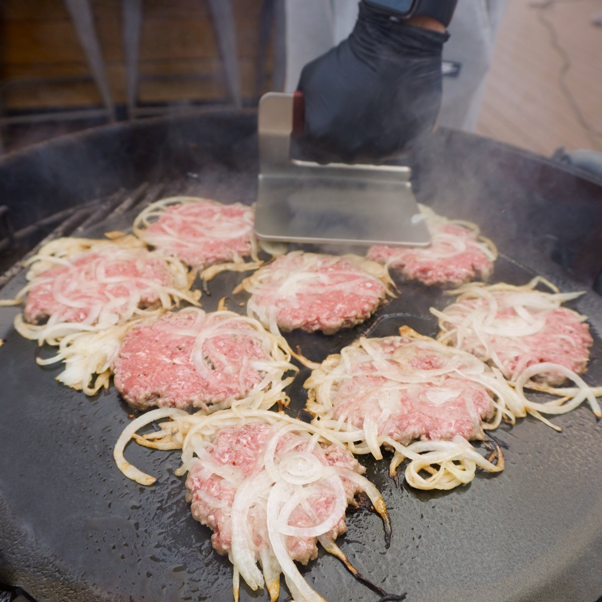 Oklahoma onion burger patties being smashed down on a griddle.