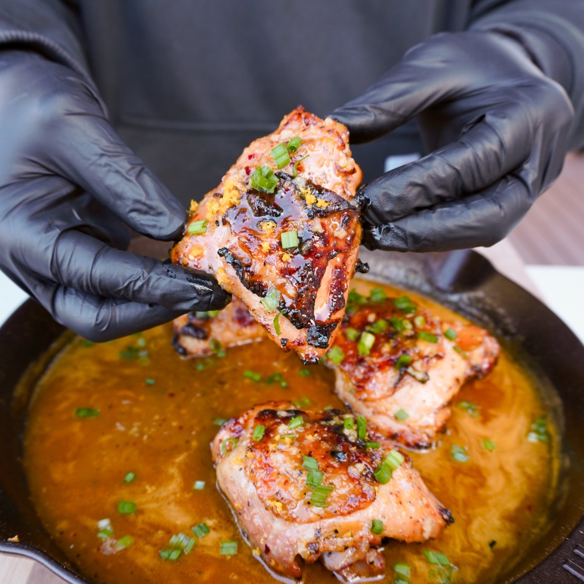 grilled orange chicken thigh being raised over skillet. 