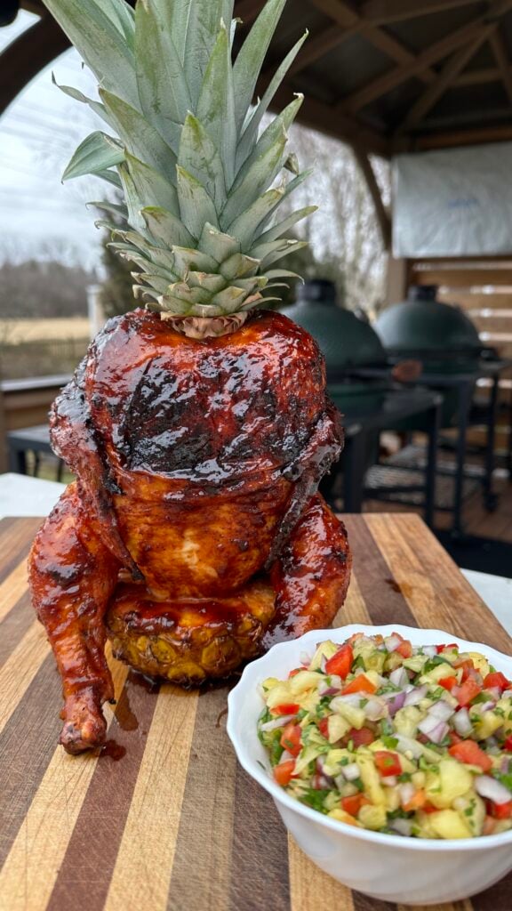 Pineapple Throne Chicken on a cutting board with a bowl of pineapple salsa. 