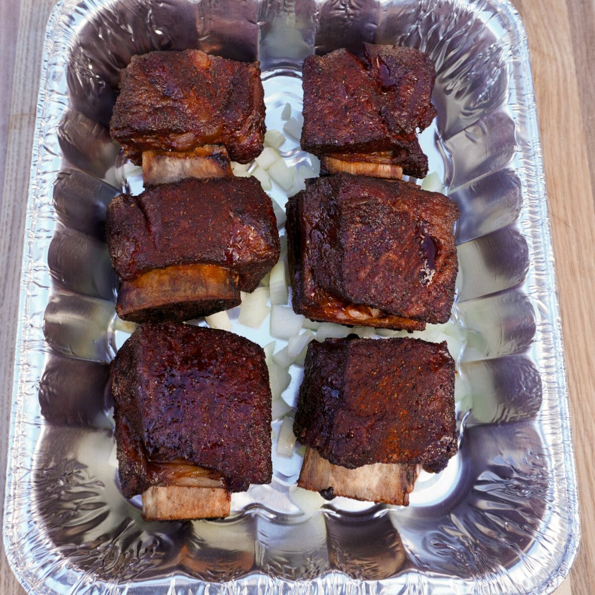 beef short ribs in a foil pan on a bed onions.