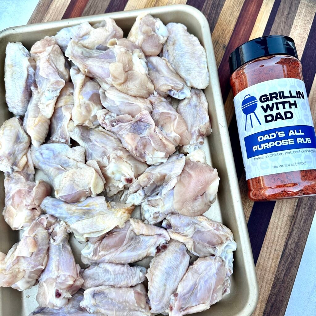 raw party wings on a metal tray with a bottle of Dad's All Purpose rub next to it.