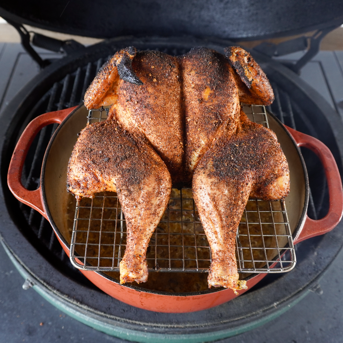 spatchcocked chicken on a wire rack on top of a dutch oven on the grill. 